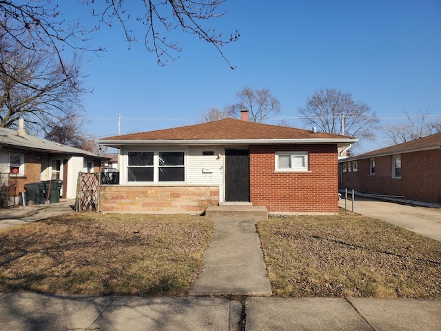 bungalow-style home featuring a front lawn, brick siding, roof with shingles, and a chimney