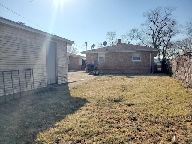 rear view of property with brick siding, a lawn, a chimney, and fence