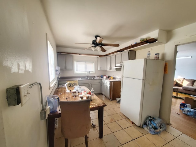 kitchen with a sink, under cabinet range hood, freestanding refrigerator, light tile patterned floors, and ceiling fan