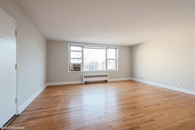 unfurnished room with cooling unit, baseboards, radiator heating unit, and light wood finished floors