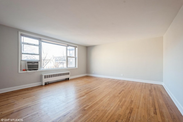 spare room featuring radiator heating unit, cooling unit, baseboards, and light wood finished floors