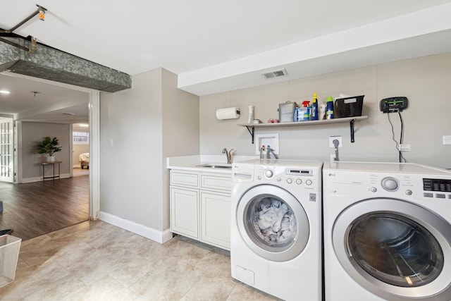 washroom featuring washing machine and clothes dryer, visible vents, baseboards, cabinet space, and a sink