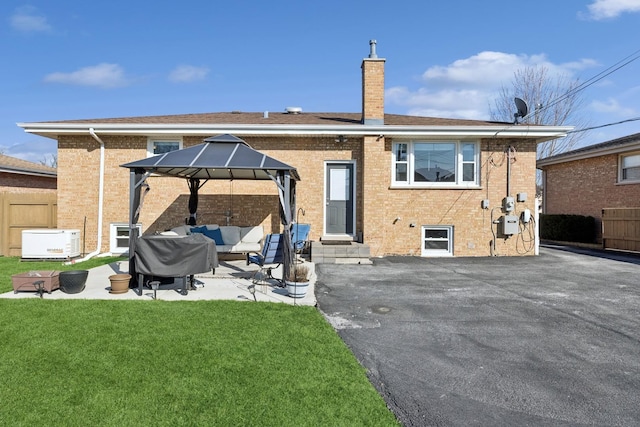 back of house with a yard, a chimney, entry steps, a gazebo, and brick siding