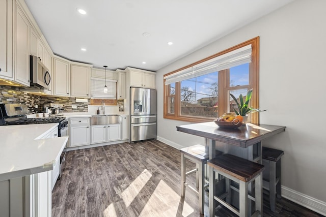 kitchen featuring light countertops, decorative backsplash, appliances with stainless steel finishes, dark wood-style floors, and a sink