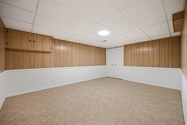 unfurnished room featuring wood walls, a paneled ceiling, and baseboards