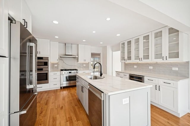 kitchen featuring wall chimney range hood, light wood-type flooring, white cabinets, stainless steel appliances, and a sink