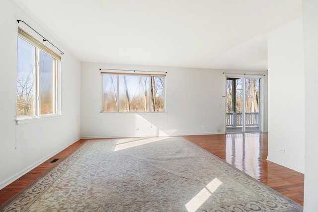 unfurnished room featuring plenty of natural light, baseboards, visible vents, and wood finished floors