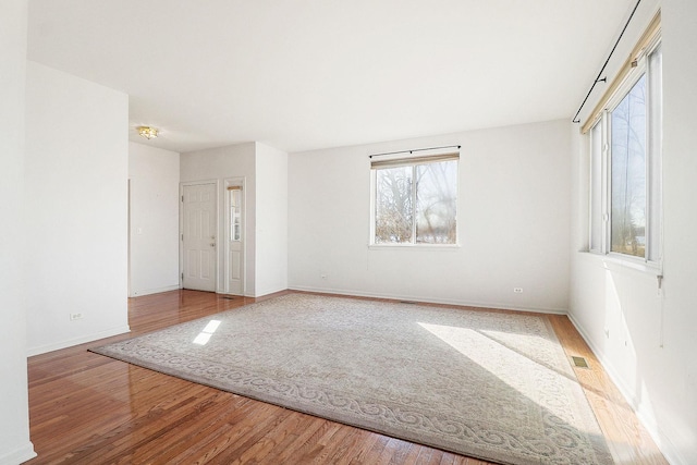 empty room with wood finished floors, visible vents, and baseboards