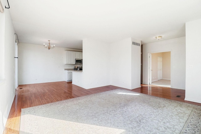 unfurnished living room with visible vents, an inviting chandelier, and wood finished floors