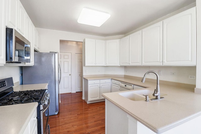 kitchen featuring a sink, dark wood finished floors, stainless steel appliances, a peninsula, and white cabinets