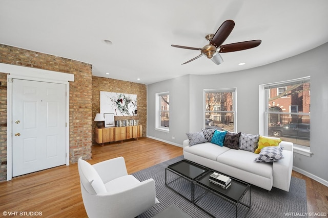 living room featuring ceiling fan, brick wall, baseboards, and wood finished floors