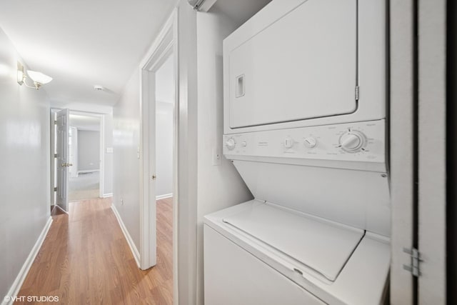 clothes washing area featuring light wood finished floors, laundry area, stacked washing maching and dryer, and baseboards