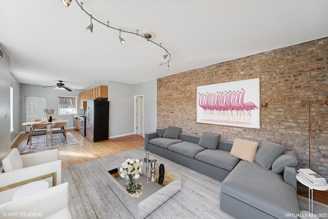 living room with track lighting, brick wall, baseboards, light wood-style floors, and a ceiling fan