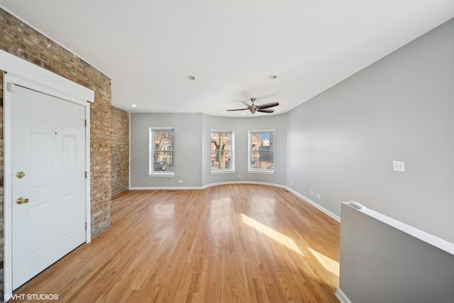 spare room featuring brick wall, a ceiling fan, baseboards, and light wood finished floors