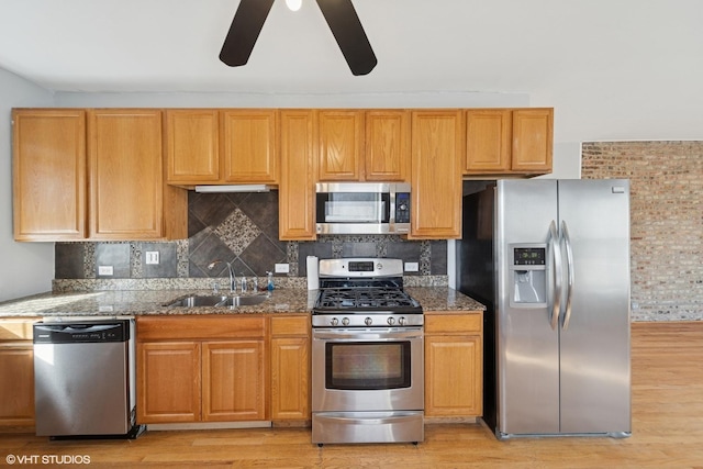 kitchen featuring tasteful backsplash, light wood-type flooring, stone countertops, stainless steel appliances, and a sink