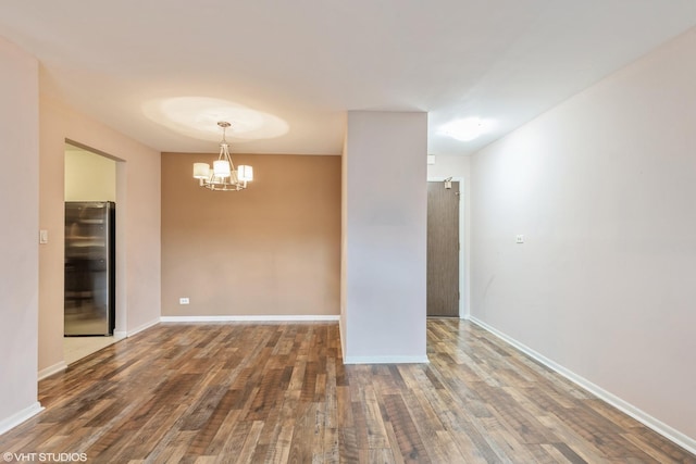 spare room featuring a notable chandelier, wood finished floors, and baseboards