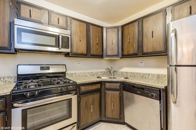 kitchen with dark brown cabinetry, light stone counters, light tile patterned floors, stainless steel appliances, and a sink