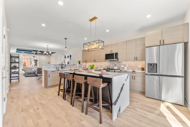 kitchen with a sink, a kitchen breakfast bar, appliances with stainless steel finishes, light wood finished floors, and decorative backsplash