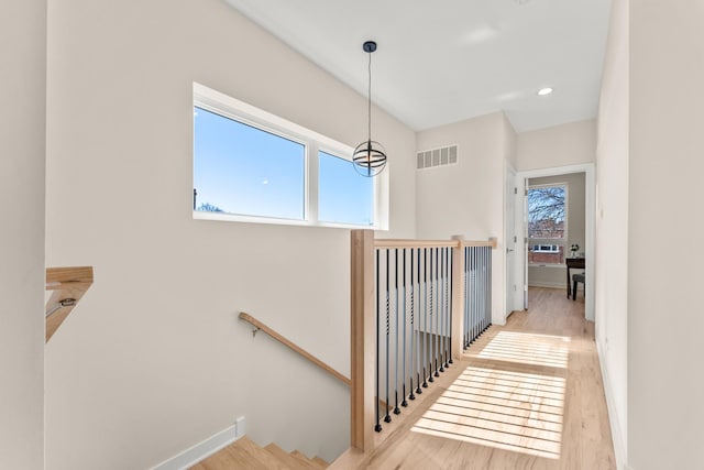 hall with visible vents, an upstairs landing, baseboards, and wood finished floors