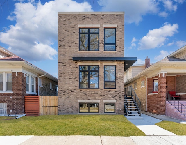 modern home with brick siding, a front yard, and fence