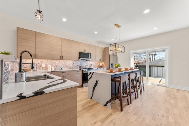 kitchen featuring light wood-type flooring, a breakfast bar, a sink, appliances with stainless steel finishes, and decorative backsplash