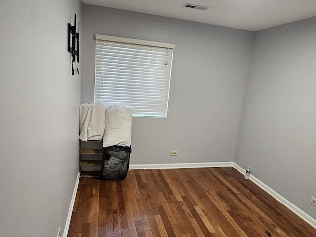 empty room with dark wood finished floors, visible vents, and baseboards