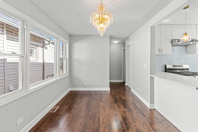 unfurnished dining area featuring dark wood finished floors, an inviting chandelier, baseboards, and visible vents