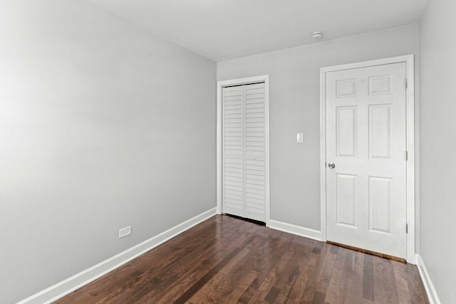 unfurnished bedroom featuring baseboards, dark wood-style flooring, and a closet