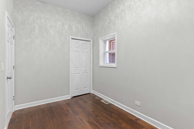 unfurnished room featuring visible vents, dark wood-style floors, and baseboards