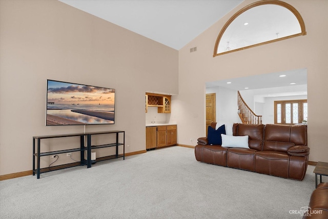 living area featuring stairway, visible vents, baseboards, a towering ceiling, and light colored carpet