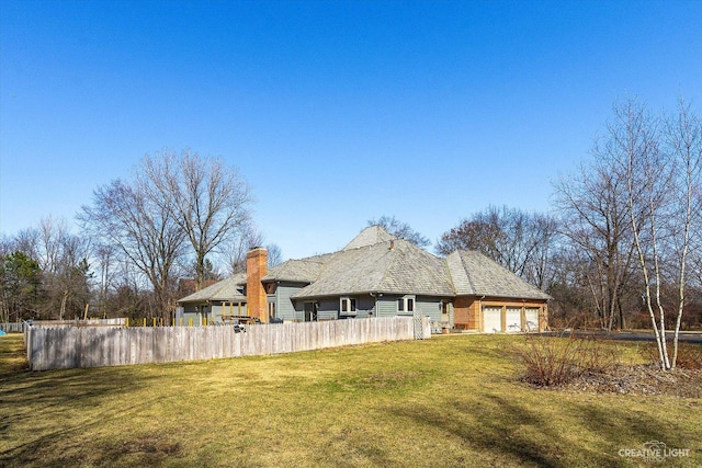 rear view of house featuring a garage, a lawn, and fence