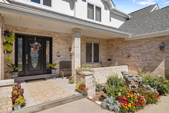 doorway to property with a porch, brick siding, board and batten siding, and roof with shingles