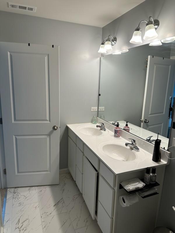 full bath featuring a sink, visible vents, marble finish floor, and double vanity