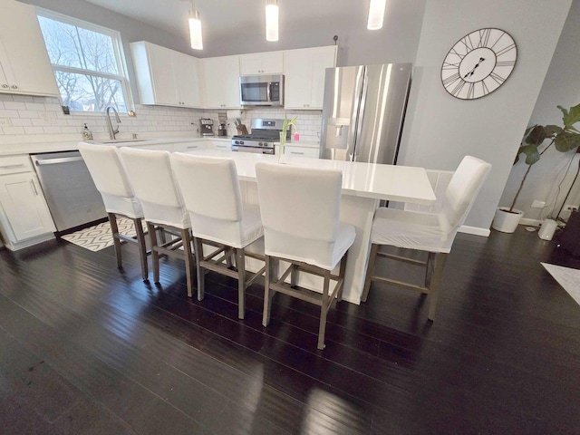 kitchen featuring dark wood-style flooring, a sink, decorative backsplash, stainless steel appliances, and a center island