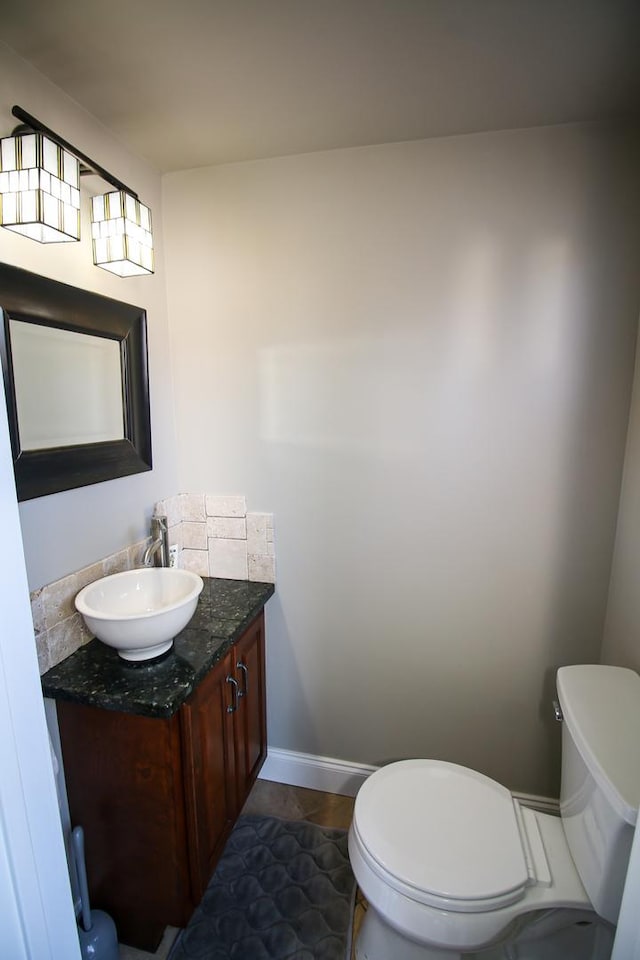 half bath with baseboards, toilet, and vanity