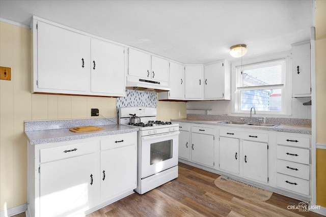 kitchen featuring white range with gas cooktop, under cabinet range hood, a sink, wood finished floors, and white cabinets