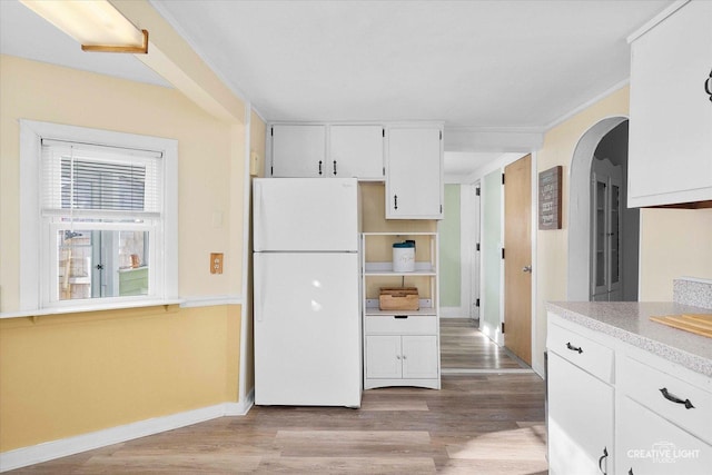 kitchen with crown molding, light wood-type flooring, freestanding refrigerator, arched walkways, and white cabinets