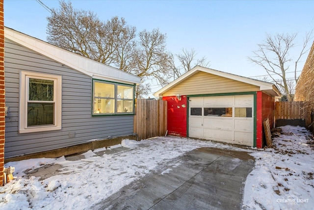 snow covered garage with a detached garage and fence