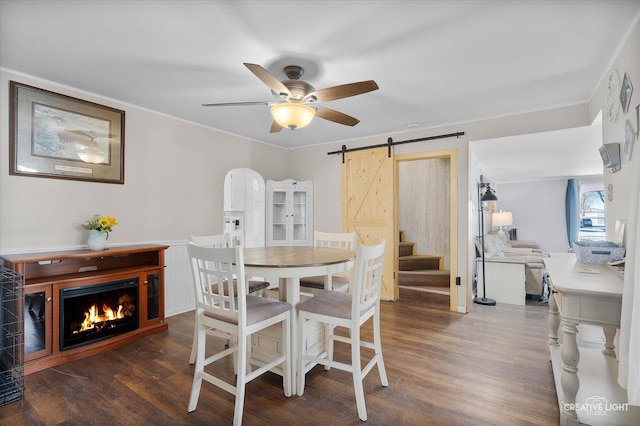 dining room featuring a barn door, wood finished floors, arched walkways, and a lit fireplace