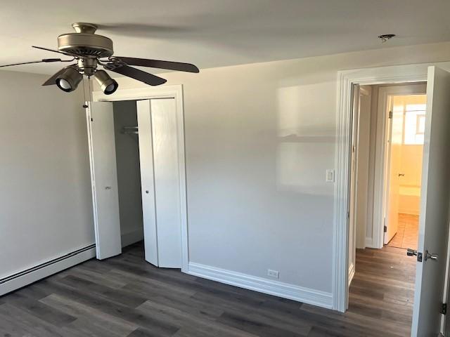 unfurnished bedroom with a closet, baseboards, baseboard heating, and dark wood-style floors