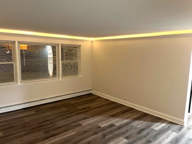 empty room with dark wood finished floors, a baseboard heating unit, and baseboards