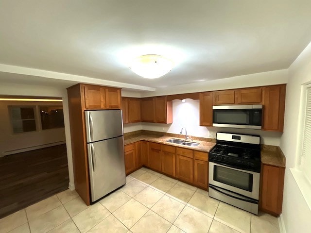 kitchen featuring a sink, light tile patterned floors, appliances with stainless steel finishes, brown cabinetry, and a baseboard radiator