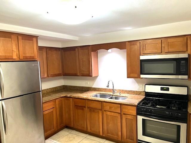 kitchen with brown cabinetry, appliances with stainless steel finishes, light tile patterned flooring, and a sink