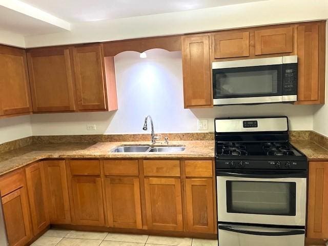 kitchen with brown cabinets, a sink, stone countertops, stainless steel appliances, and light tile patterned floors