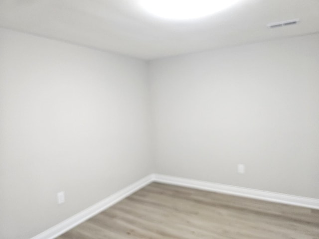 empty room with light wood-style floors, visible vents, and baseboards