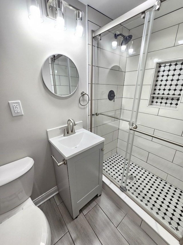 bathroom with toilet, vanity, a shower stall, baseboards, and wood tiled floor