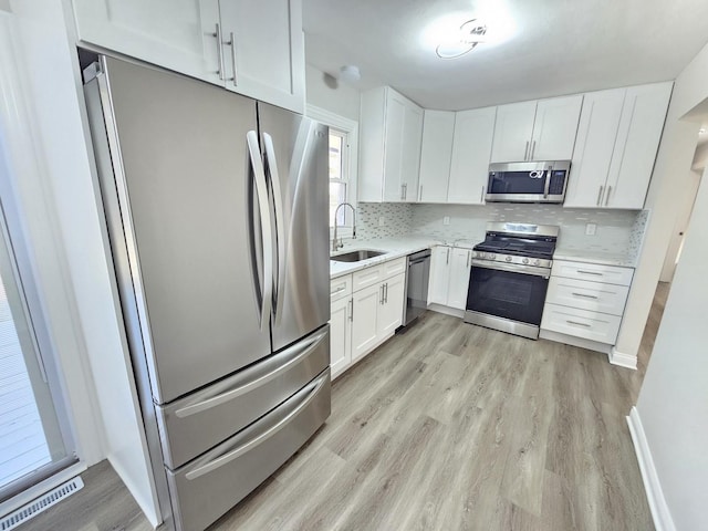 kitchen with a sink, light countertops, appliances with stainless steel finishes, white cabinetry, and light wood-type flooring