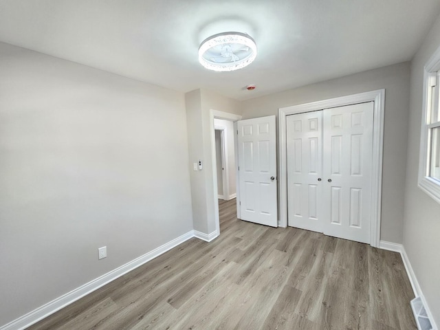 unfurnished bedroom with light wood-style floors, baseboards, visible vents, and a closet