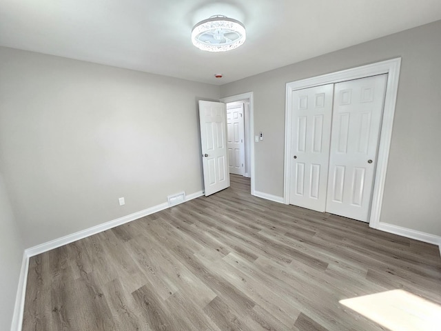 unfurnished bedroom featuring a closet, visible vents, baseboards, and wood finished floors