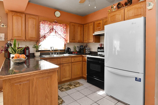 kitchen featuring gas stove, a peninsula, freestanding refrigerator, a sink, and under cabinet range hood